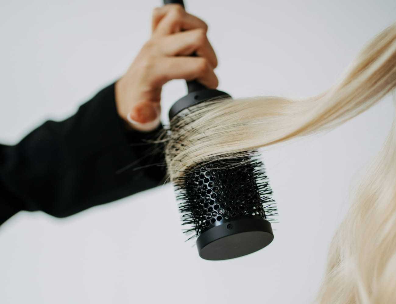 Hairstylist using round brush on long blonde hair.