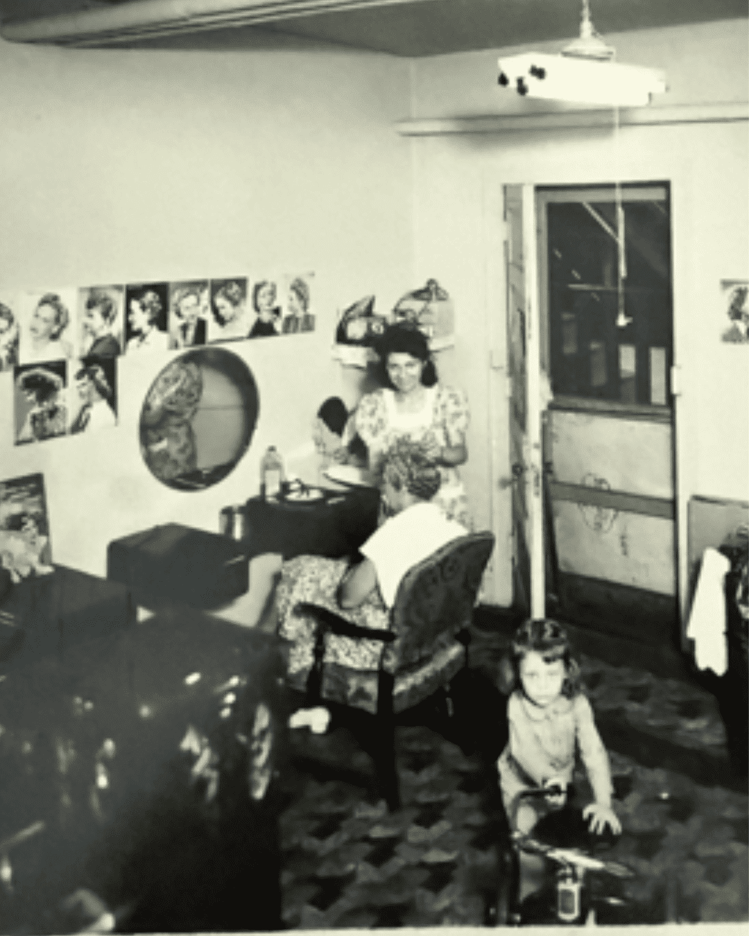 Vintage salon with women styling hair, young girl playing on floor. Retro posters on walls.